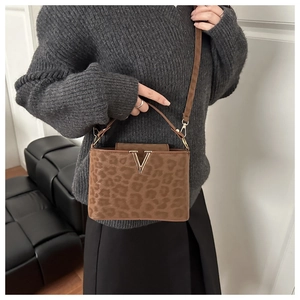 Détail d'un sac à bandoulière léopard avec boucle dorée en V et texture douce en velours