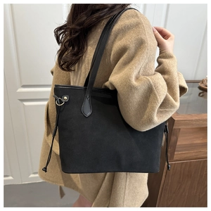Detail of black suede tote bag with drawstring and gold hardware worn with camel coat