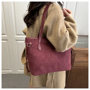 Detail view of large burgundy suede tote bag styled with a camel coat in a modern setting