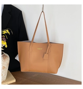 Détail du sac cabas en similicuir marron avec logo doré à côté d'un costume noir