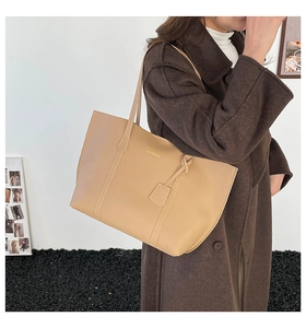 Detail of a large beige tote bag worn with a wool coat for elegant urban commuting