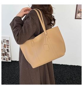 Minimalist khaki leather tote bag with long shoulder straps worn by model against a white wall