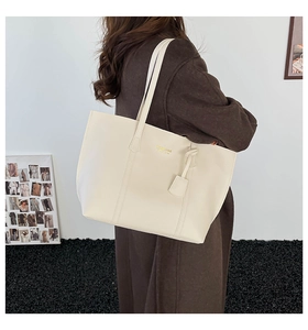 Close-up of a large cream white PU leather tote bag worn over a dark wool coat