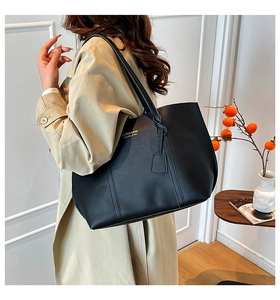 Détail d'un grand sac cabas noir minimaliste avec logo doré porté à l'épaule