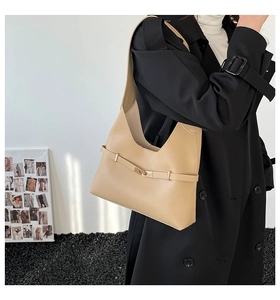 Dettaglio di borsa a spalla in pelle beige con fibbia dorata su un cappotto nero