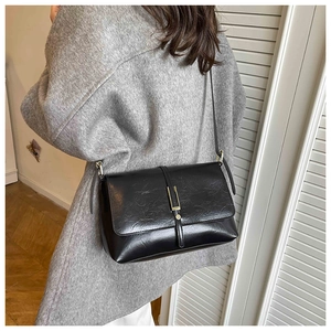 Back view of model wearing a black pleated faux leather crossbody bag with clasp detail