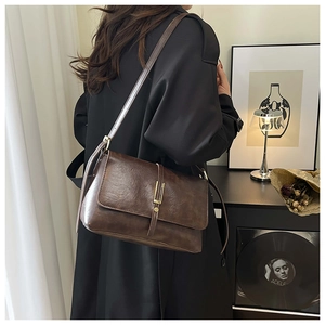 Sac bandoulière rétro en similicuir marron avec rabat porté sur un trench-coat foncé