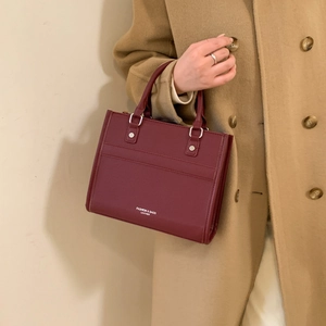 Sac cabas chic en cuir bordeaux pour femme porté avec un manteau en laine camel
