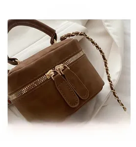 Detail view of brown suede mini bag with dual gold zippers and metal chain strap