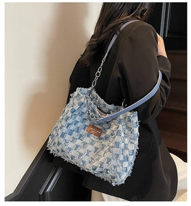Detail view of denim checkerboard shoulder bag with frayed edges and leather brand patch