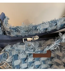Detail of distressed denim tote with frayed edges, silver zipper and leather logo patch