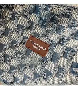 Detail of blue checkerboard denim fabric with fringe edges and brown leather logo patch