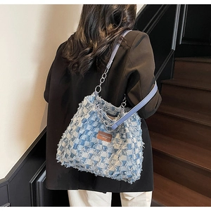 Detail of blue denim patchwork tote bag featuring frayed edges and a silver chain strap