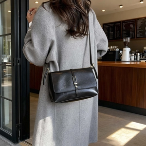 Sac bandoulière noir en cuir avec boucle dorée sur un mannequin en manteau gris clair