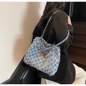 Détail du sac patchwork en denim bleu avec bords frangés, étiquette cuir et chaîne