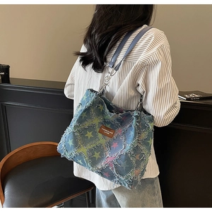 Detail of vintage denim tote featuring frayed edges, colorful stars, and metal chain strap