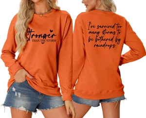 Detail of Stronger Than The Storm text print on a bright orange crewneck sweatshirt