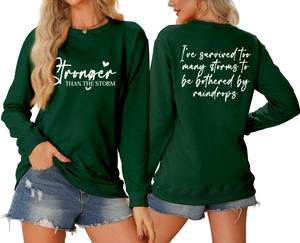 Detail of dark green sweatshirt featuring white Stronger Than The Storm printed lettering