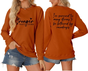 Detail of orange crewneck sweatshirt with 'Stronger THAN THE STORM' print and back text