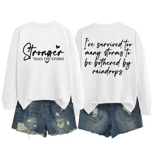 Detail view of white sweatshirt with 'Stronger THAN THE STORM' print and distressed denim shorts