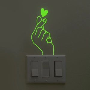 Luminous heart gesture wall sticker glowing in green on a white light switch panel