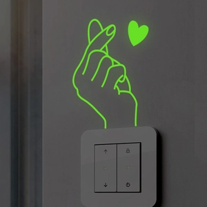 Luminous green heart gesture wall sticker glowing on a switch panel in the dark