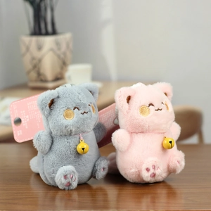 Close-up of cute plush cat keychains in grey and pink with bells on a wooden desk