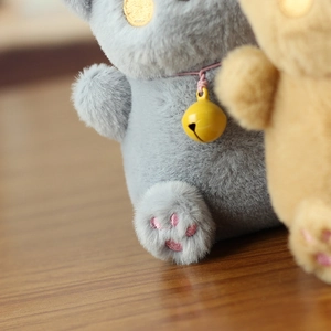 Close-up of plush lucky cat keychain with pink paw embroidery and yellow bell detail