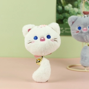Close-up of white plush cat pendant with blue embroidery and a golden metal bell detail