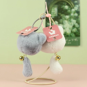 Detail of plush cat charms featuring soft fur, long tails, and golden bells on a rack