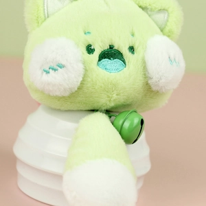 Détail d'un porte-clés chat en peluche montrant la fourrure verte et les broderies