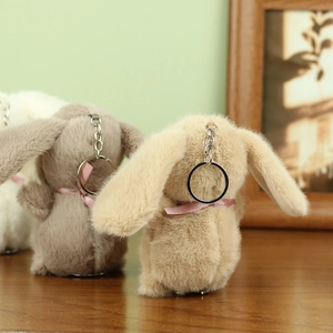 Rear view of cute plush rabbits with silk bows and silver metal keychains on wood
