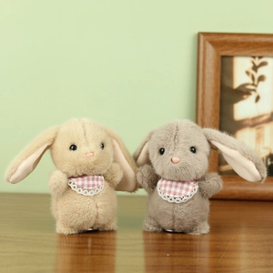 Close-up of cute plush bunny charms in beige and grey with lace bibs on a wooden desk