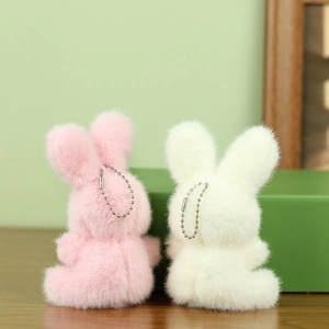 Detail van zachte roze en witte pluche konijnenhangers met zilveren kettingen op hout