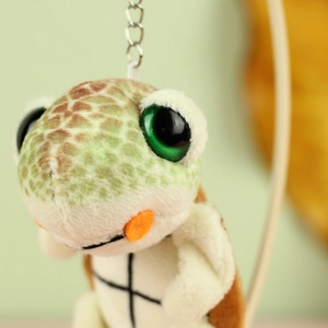 Detail of plush turtle keychain with big green eyes and soft brown textured shell
