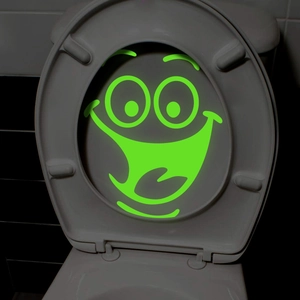 Glow in the dark cartoon smiley face sticker on a toilet lid in low light conditions