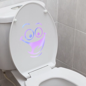 Luminous gradient cartoon smiley face sticker applied on a white toilet lid in bathroom