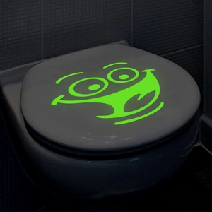 Glow-in-the-dark green cartoon smiley face sticker on dark toilet lid for bathroom decor