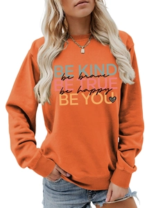 Close-up of vibrant orange sweatshirt showing Be Kind lettering and leopard heart detail