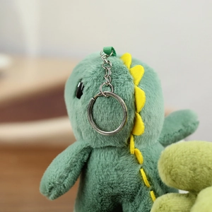 Gros plan d'un porte-clés dinosaure en peluche verte avec écailles jaunes et anneau argent