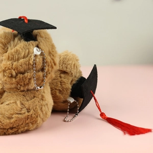 Detail of plush graduation bear keychain featuring a black doctor hat with red tassel