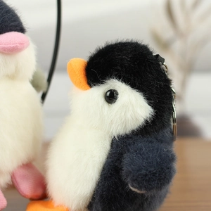 Close-up of a fluffy penguin plush keychain with soft faux fur and metal buckle on wood