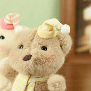 Close-up of a cute plush teddy bear wearing a yellow striped hat and matching scarf