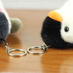 Close-up of fluffy penguin plush keychain with polished silver ring on wooden desk