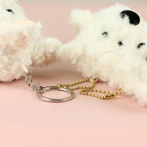 Detail of plush white puppy pendants featuring silver keyrings and gold beaded chains