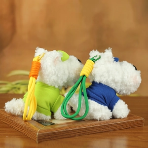 Detailed view of white Westie plush keychains in green and blue shirts on a wooden frame