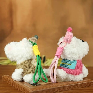 Detail of plush Westie keychains wearing brown and pink knitted sweaters on a warm background