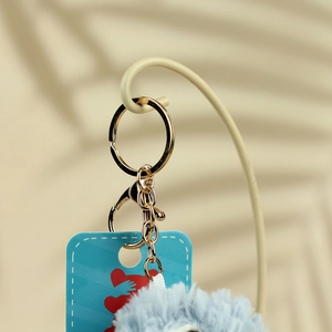 Macro view of light blue plush ball keychain with gold ring and heart pattern card
