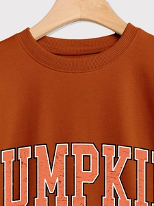 Détail d'un sweat orange citrouille avec lettrage vintage sur un cintre en bois naturel