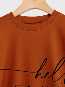 Close-up of rust red sweatshirt featuring a ribbed crew neck and hello print detail